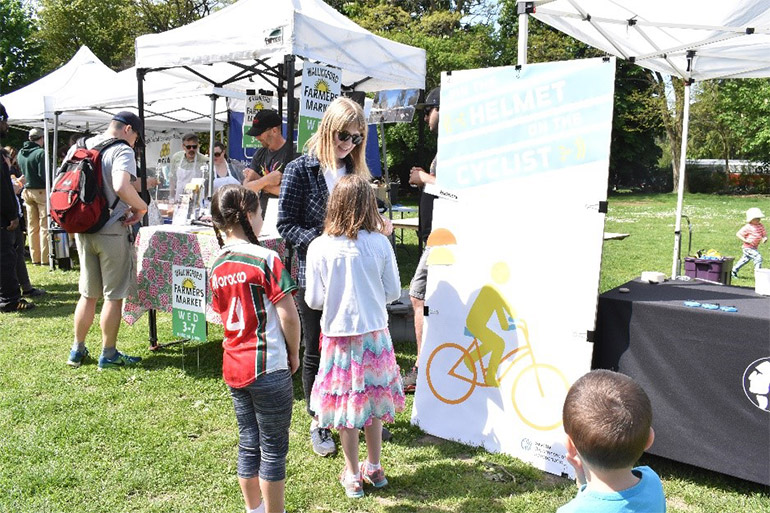 A member of our outreach team welcomes kids to the project booth while tabling at a community event on a sunny day.
